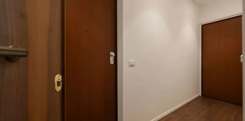 Un pasillo interior con puertas marrones y una pared clara.