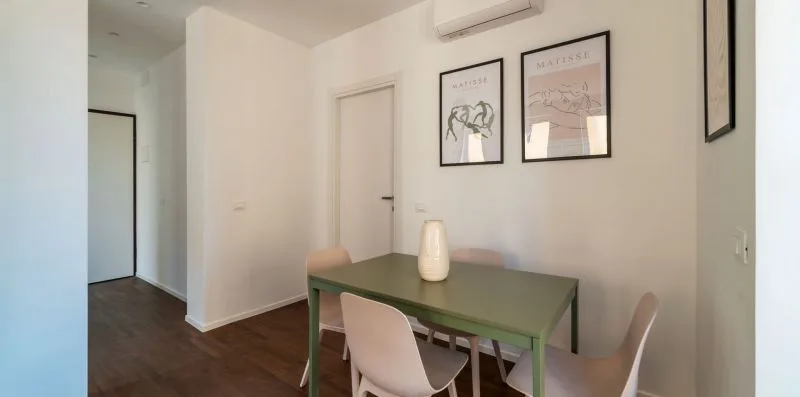 Un comedor con una mesa verde, sillas y cuadros enmarcados en la pared.