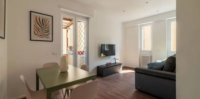 Una sala luminosa tiene una mesa de comedor, un televisor y asientos junto a las ventanas.