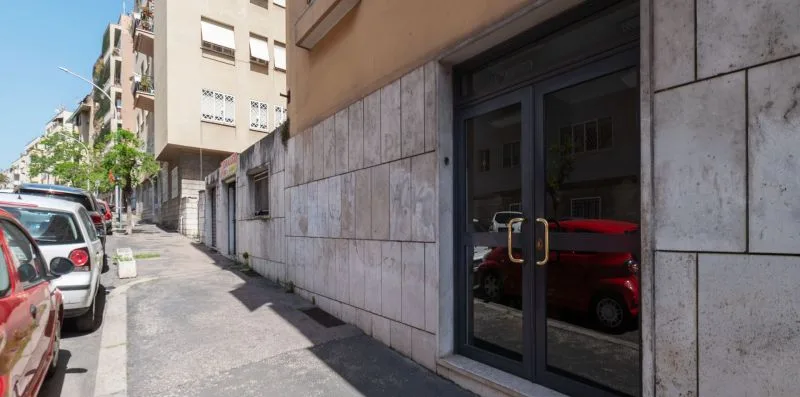 Una acera urbana bordea un edificio revestido de piedra con una entrada acristalada.
