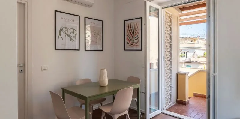 Un comedor con una mesa y sillas junto a una puerta abierta al balcón.