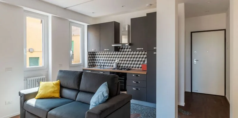 Una sala de estar con un sofá oscuro junto a una cocina compacta.
