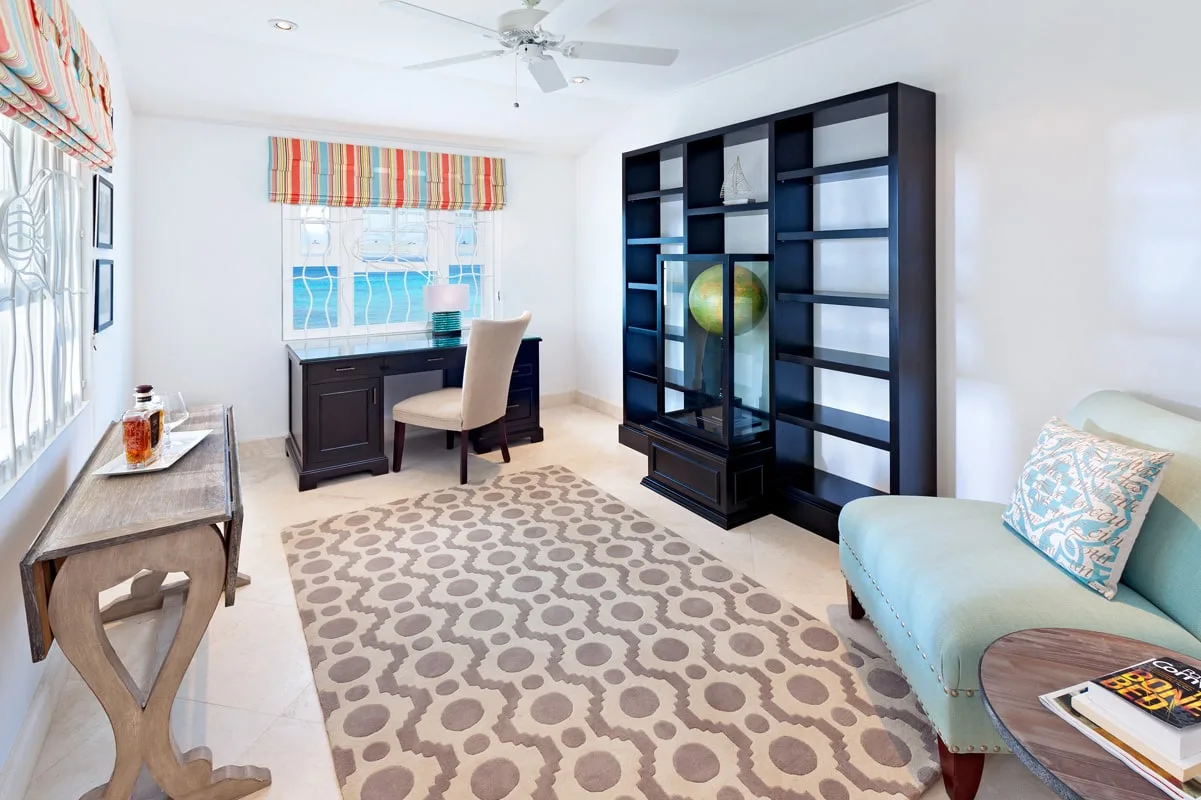 A bright room with a desk, dark shelving, and a patterned rug.