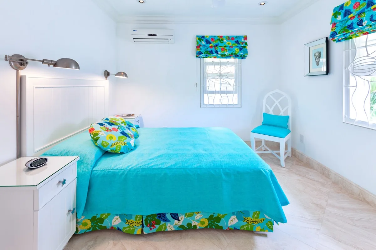 A bedroom with a turquoise bedspread and colorful patterned curtains.