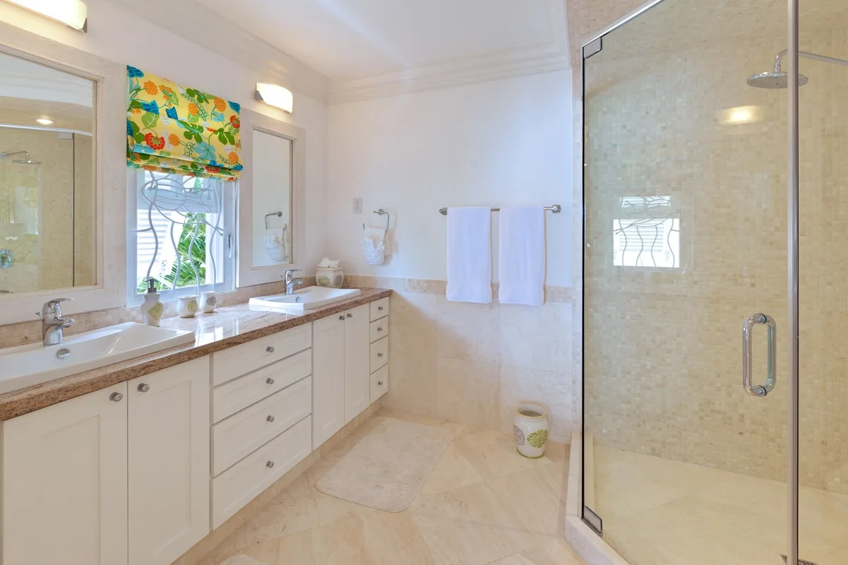 A bright bathroom with a long vanity, mirrors, and a glass shower.