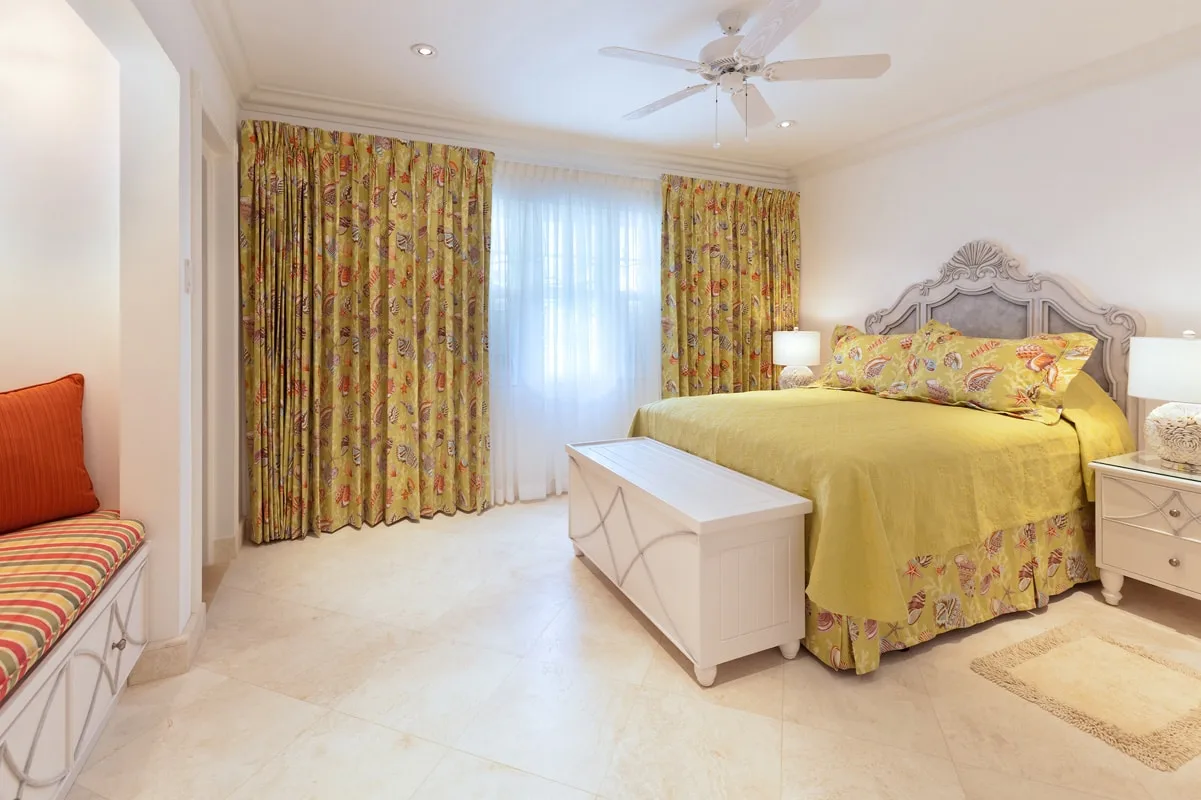 A bedroom with a yellow floral bedspread and matching curtains.
