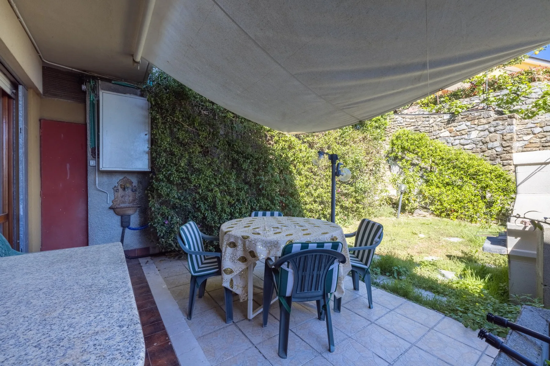A shaded outdoor dining area with a round table and surrounding seating.
