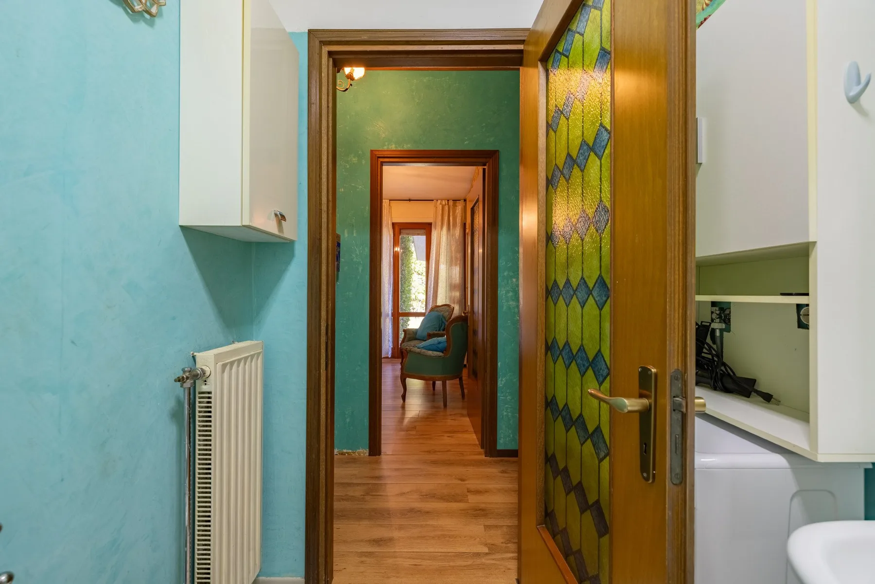 A hallway with an open patterned-glass door and a view into a sitting room.