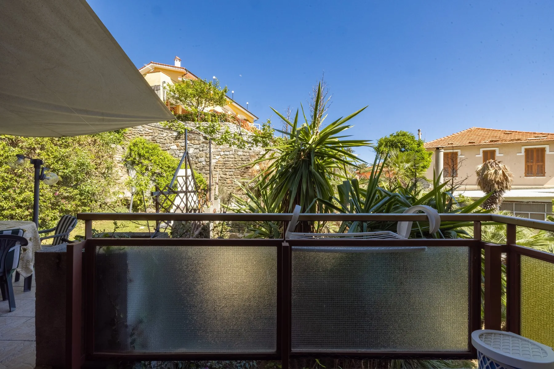 An outdoor patio with a shaded seating area and leafy plants.