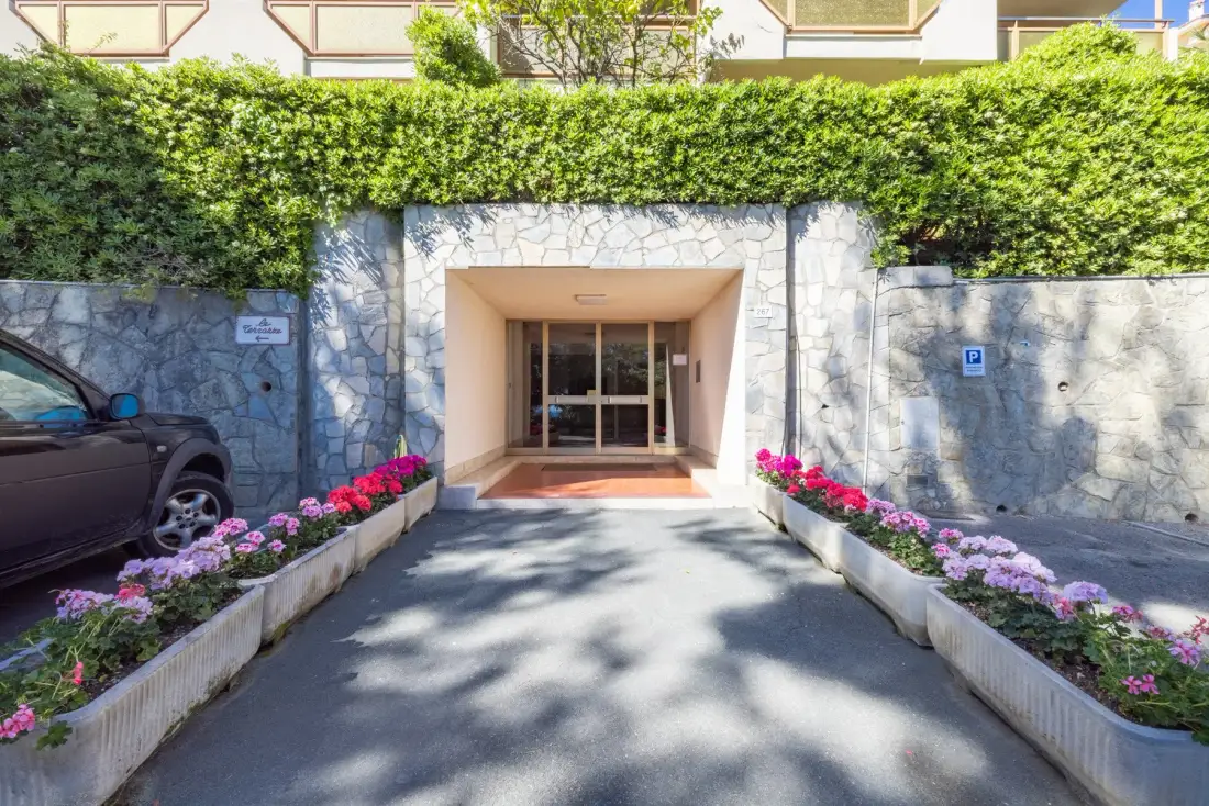 A building entrance framed by stone walls, greenery, and flower beds.
