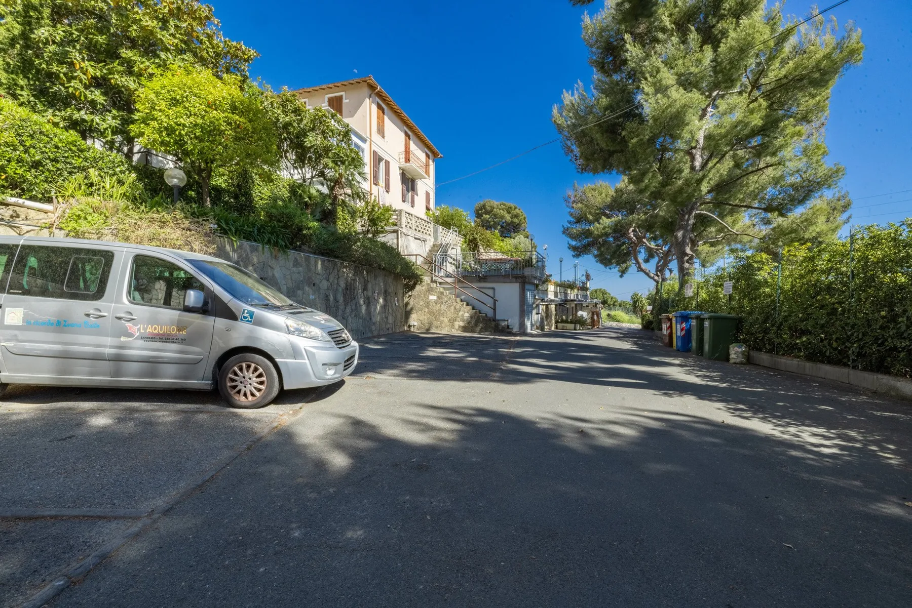 A paved driveway runs past a parked van toward a house among trees.