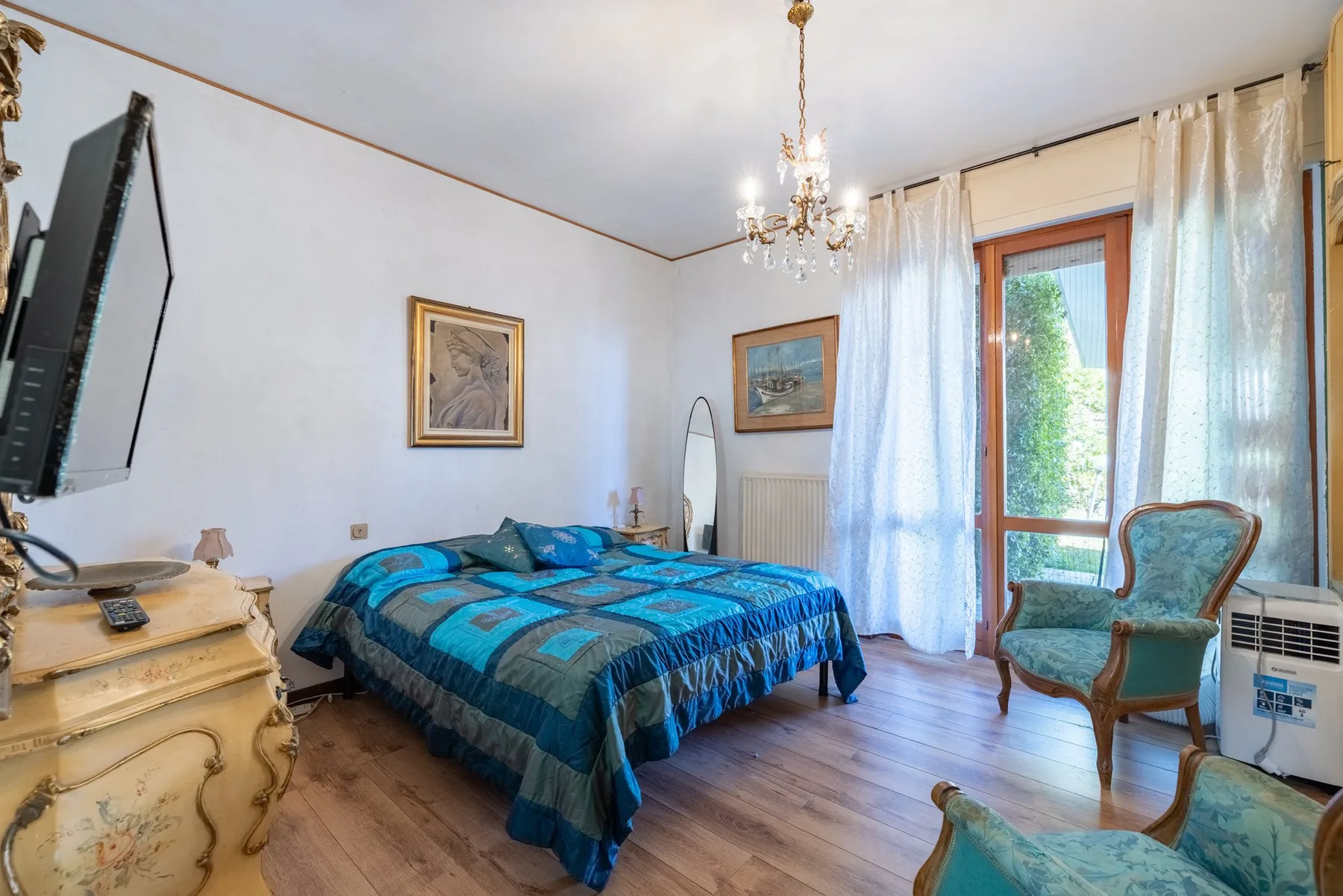 A bedroom with a blue bed, a chandelier, and a curtained glass door.