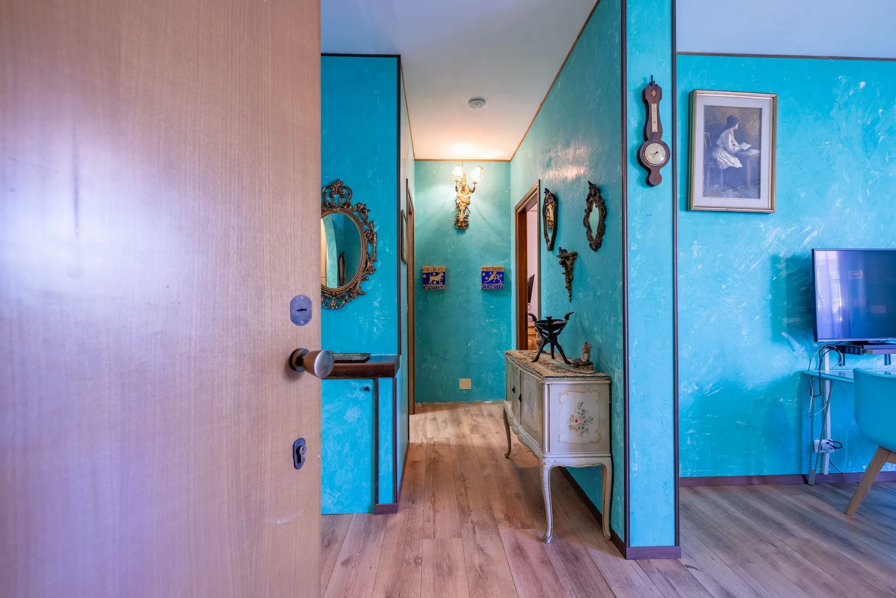 A turquoise hallway opens into a room with framed artwork and decorative furnishings.