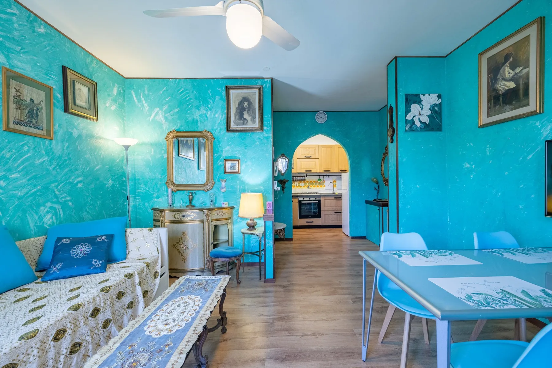 A colorful living and dining area with turquoise walls and an arched opening to the kitchen.