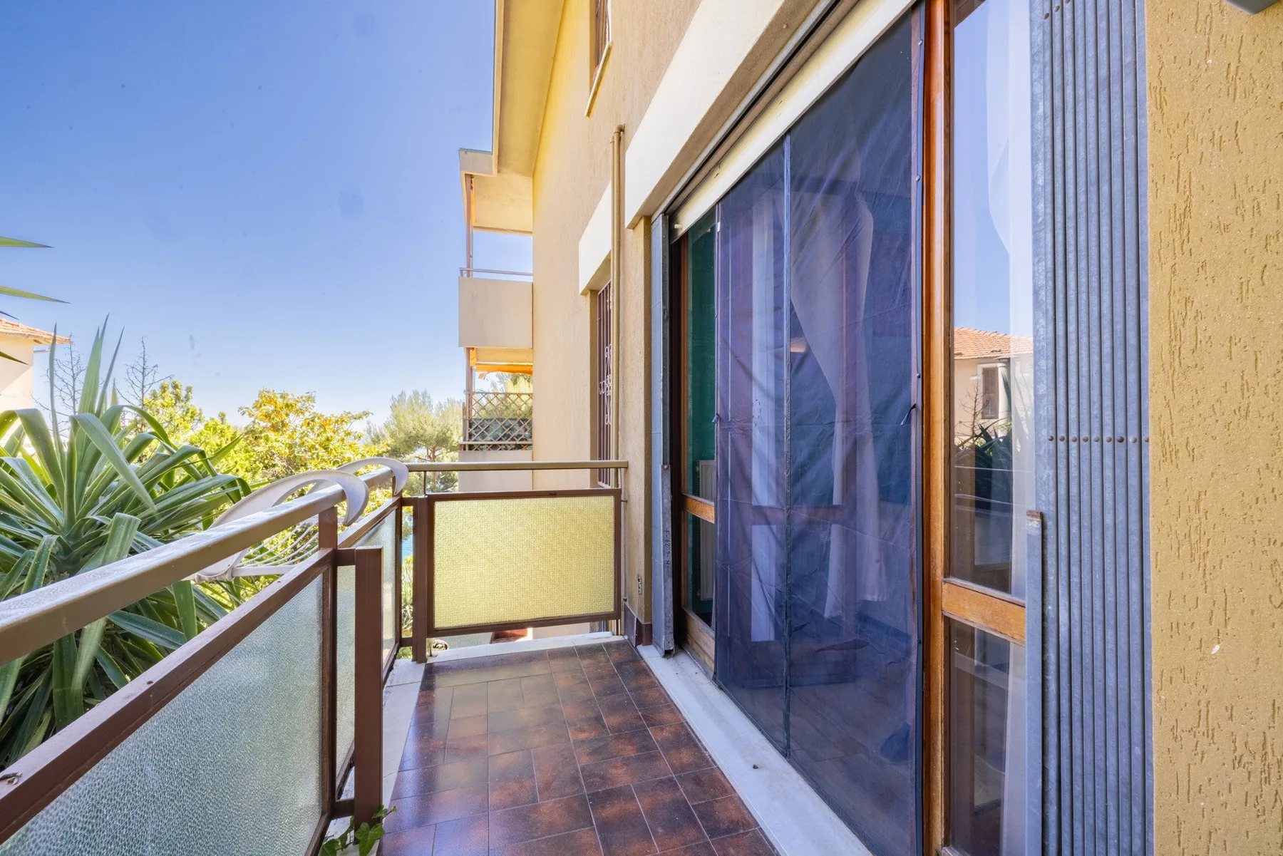 A narrow balcony with tiled flooring, a railing, and glass doors.