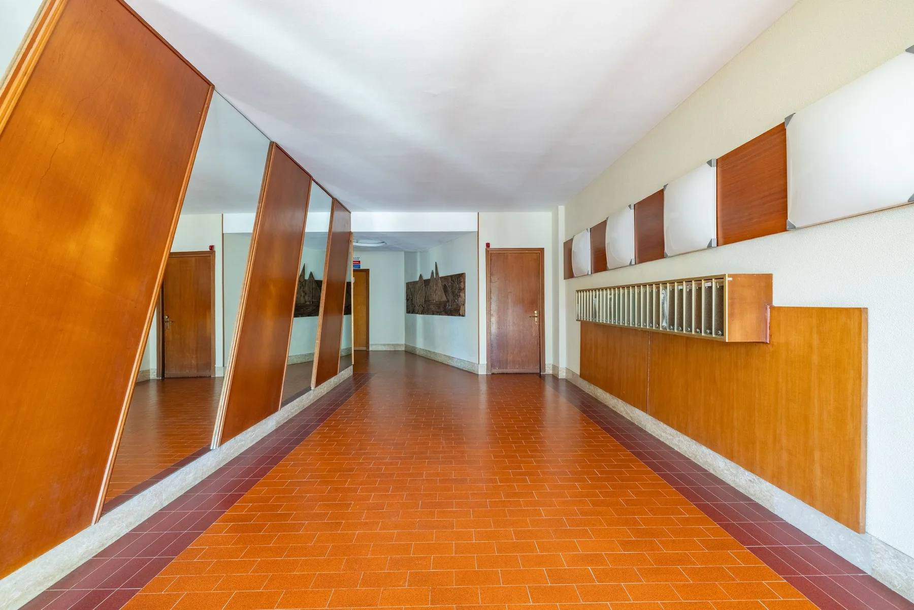 A long interior hallway with terracotta-colored tile flooring and wooden wall panels.