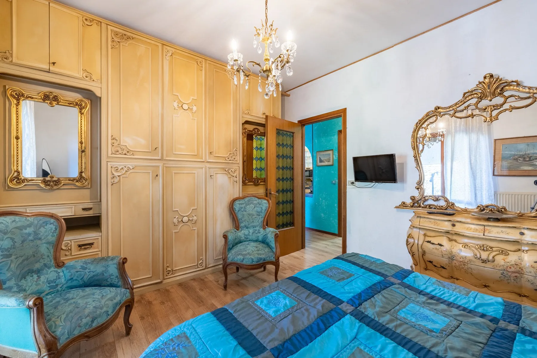 A bedroom with a blue patterned bedspread, ornate furnishings, and a wall-mounted television.