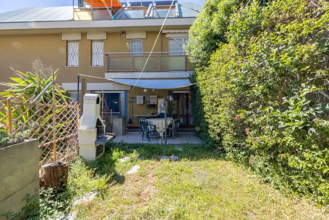 A small garden patio with outdoor seating sits beside a two-story building.