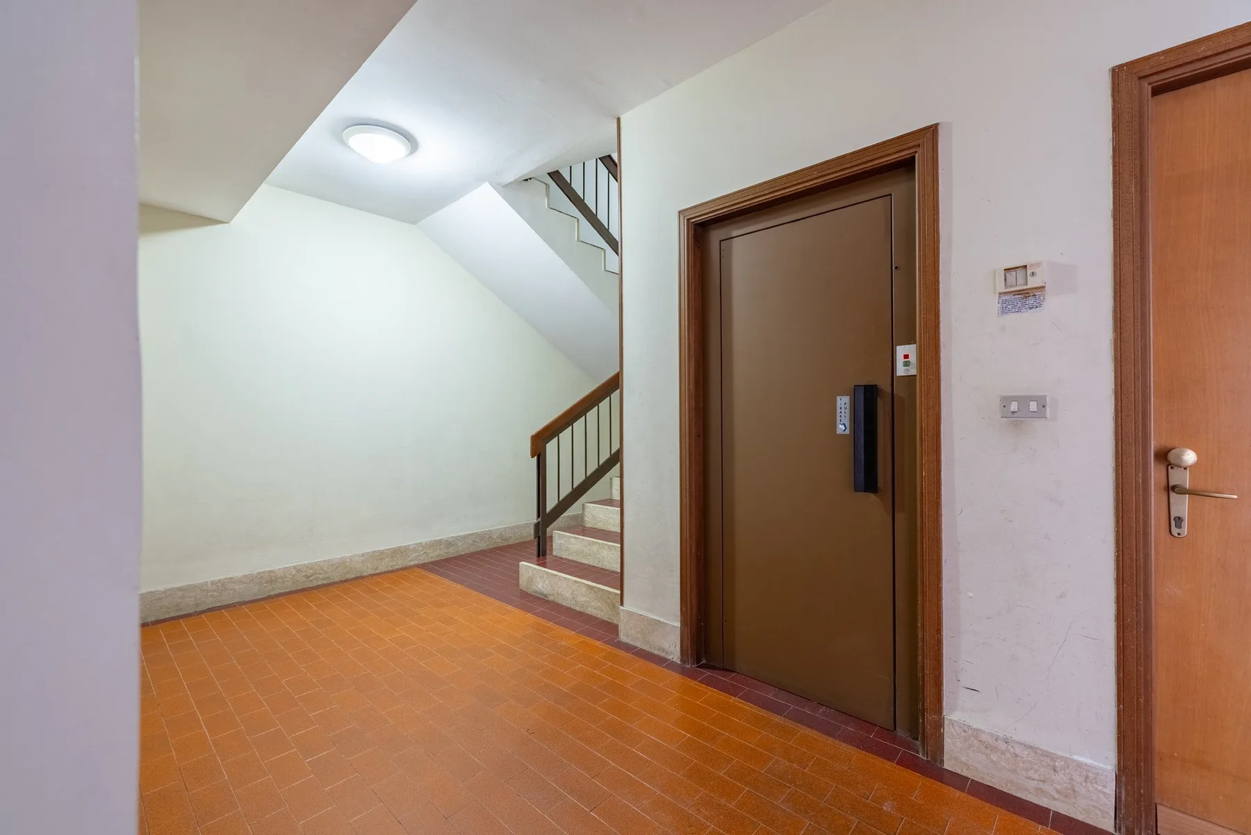 An indoor hallway with a staircase beside a brown door.