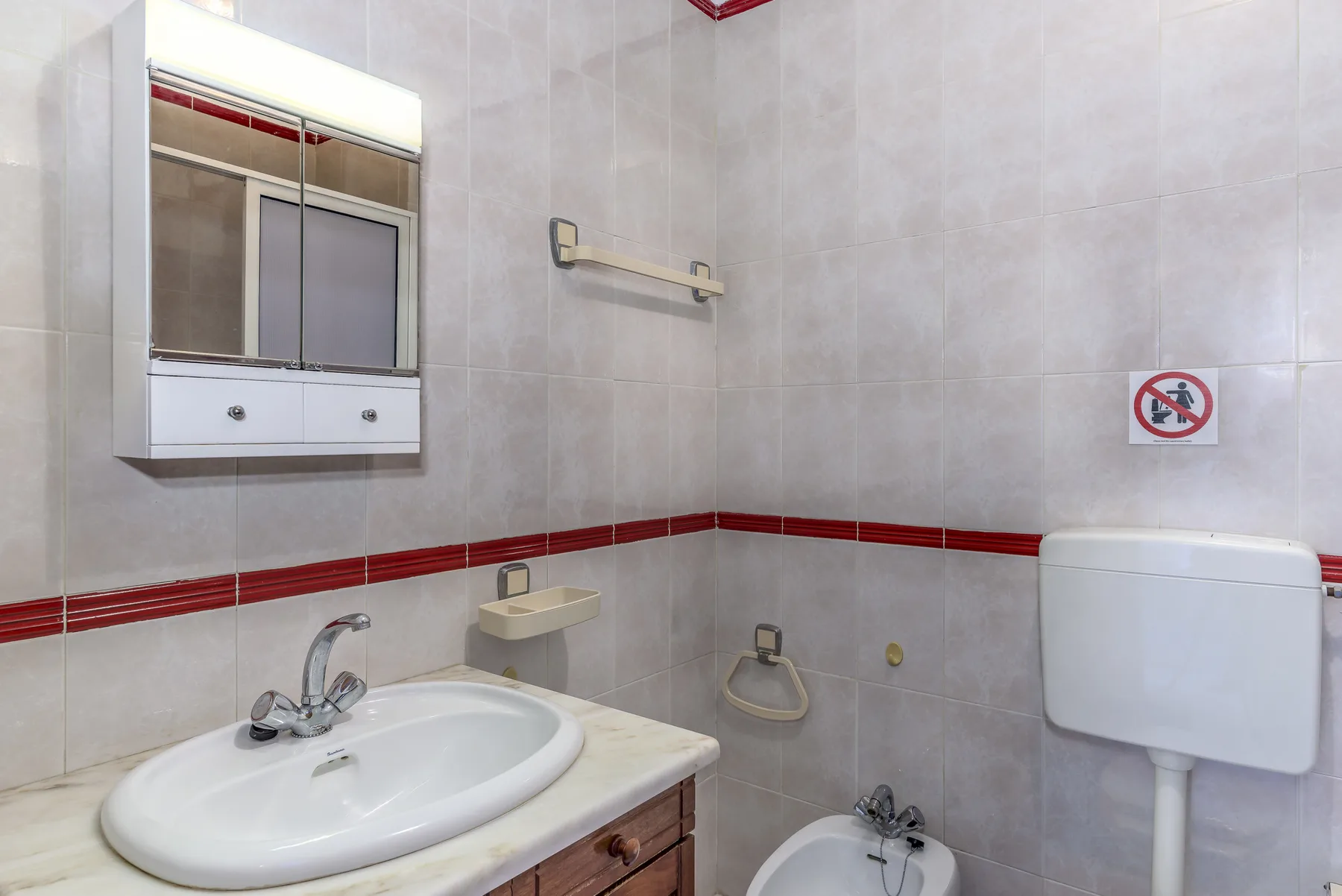 Un baño con azulejos, lavabo, armario con espejo e inodoro.