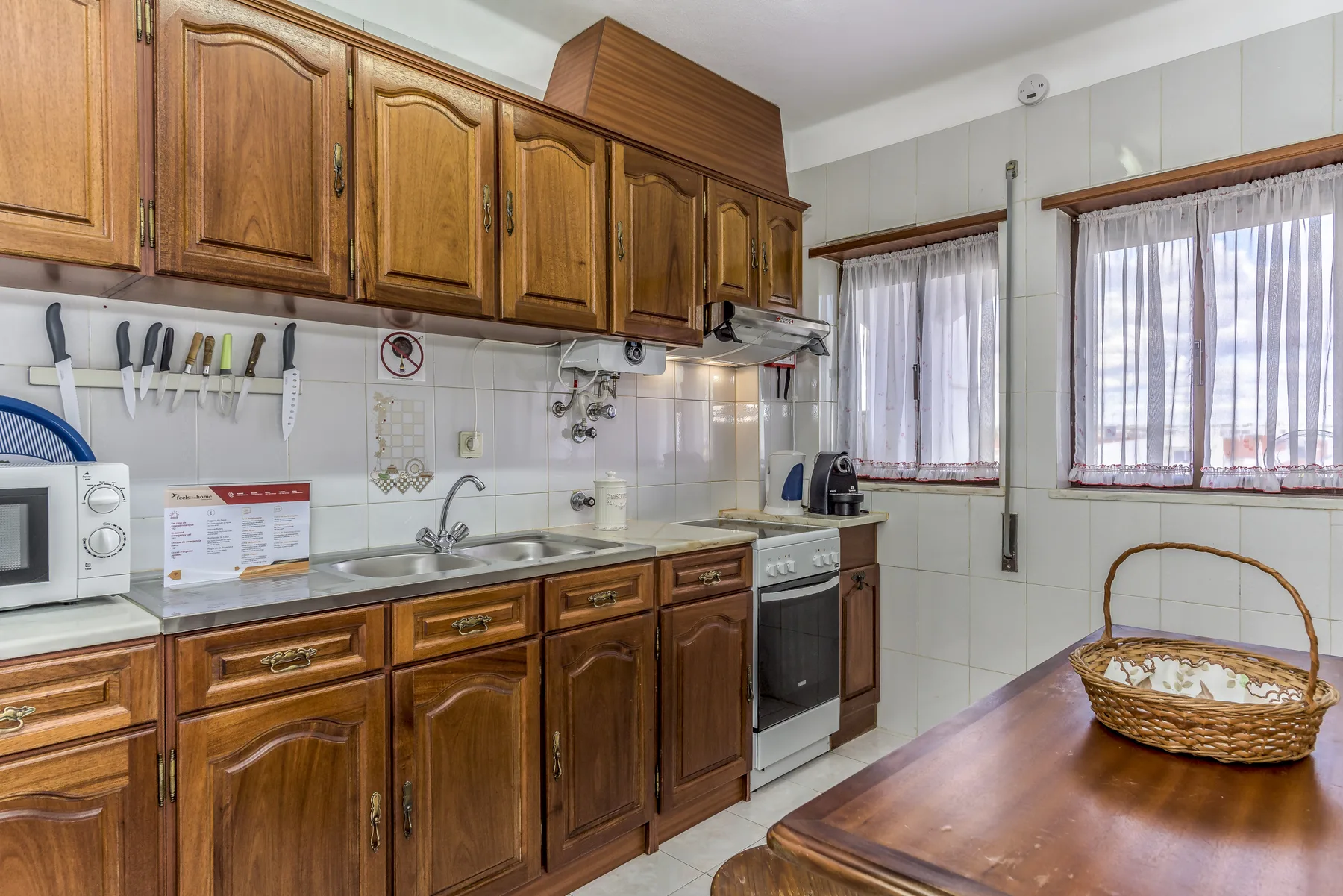 Una cocina con armarios de madera, paredes de azulejos y una mesa junto a las ventanas.