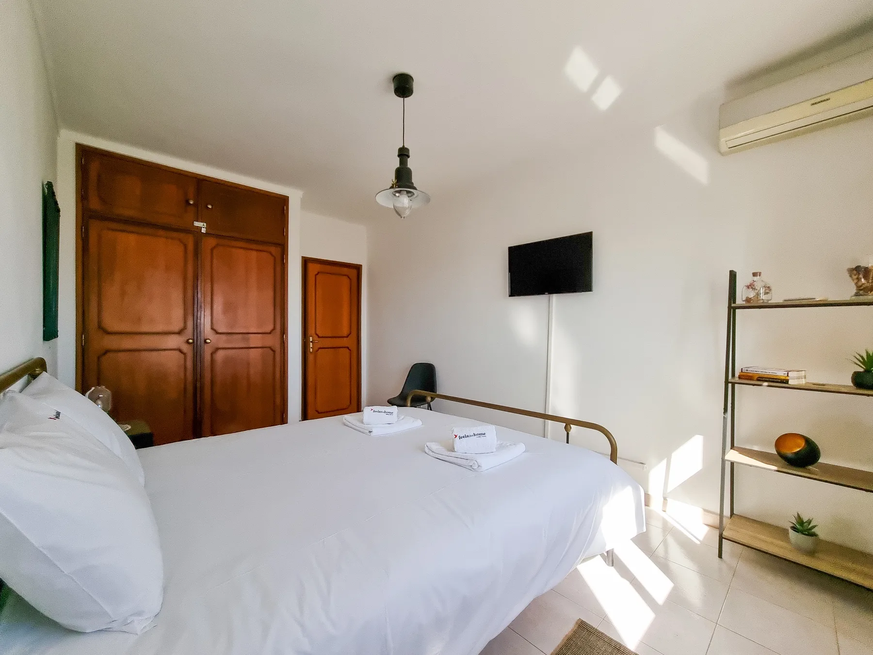 Un dormitorio con una cama grande, un televisor en la pared y estanterías abiertas.