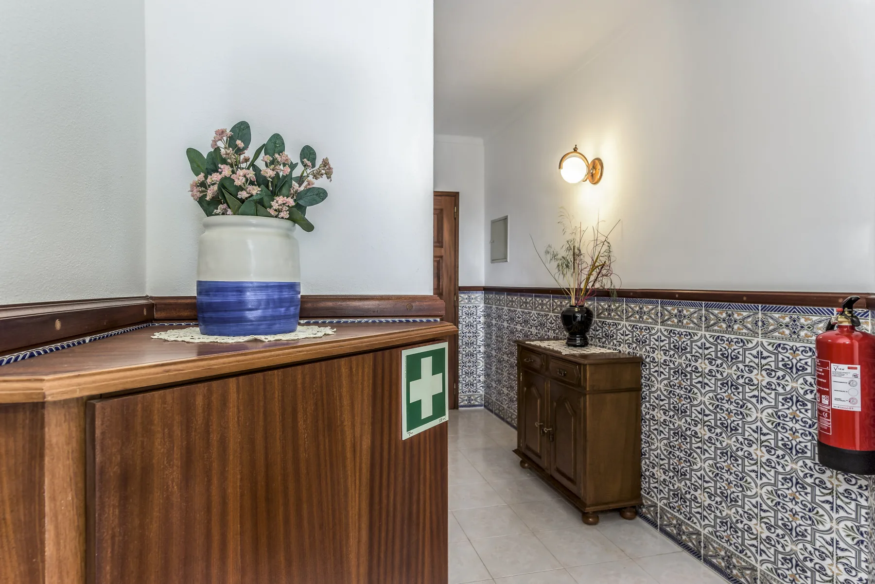 Pasillo con azulejos, muebles de madera y un extintor en la pared.