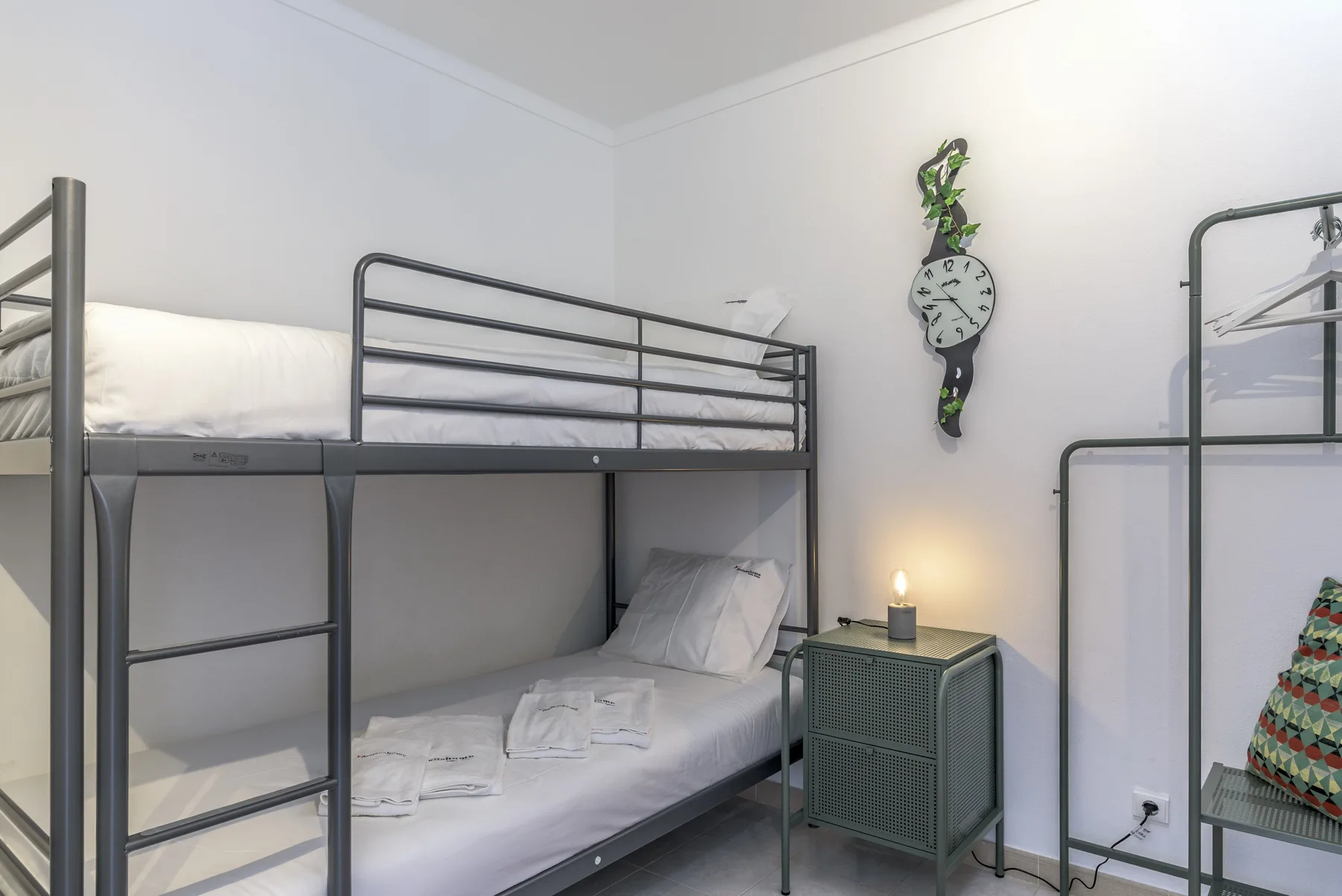 Un dormitorio luminoso con literas metálicas y ropa de cama blanca bien arreglada.