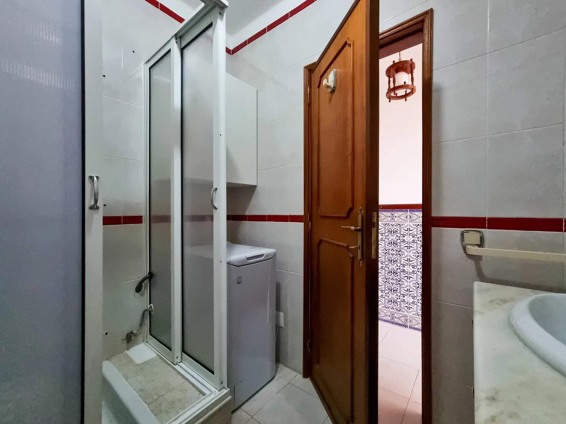 Un baño con azulejos, ducha de vidrio, lavadora y puerta de madera abierta.