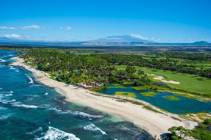 Vista aérea de una costa tropical con una playa de arena y campos verdes tierra adentro.