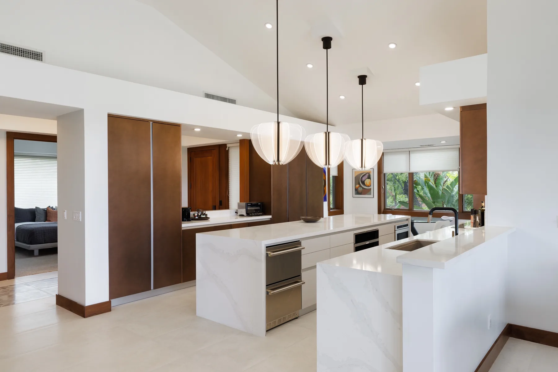 Una cocina moderna con una isla blanca, gabinetes de madera oscura y luces colgantes.