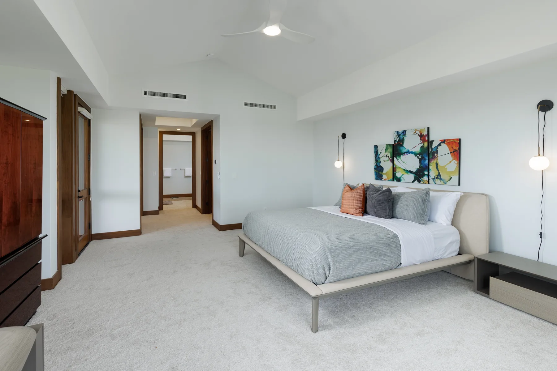 Un dormitorio luminoso con una cama tendida y cuadros coloridos encima.