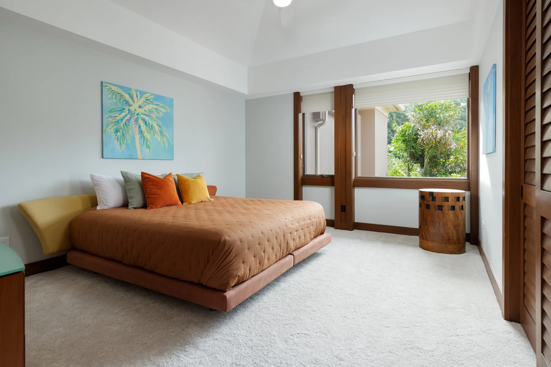 Un dormitorio luminoso con una cama, almohadas de colores y una ventana grande.