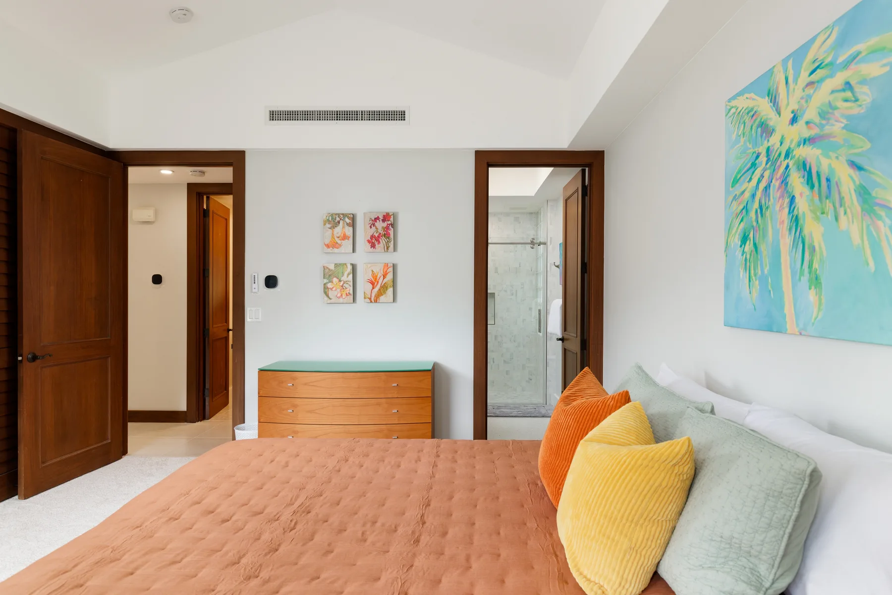 Un dormitorio con una cama, cojines de colores y una puerta al baño.