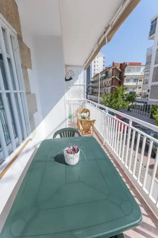 Un balcón soleado con una mesa verde de exterior y edificios de apartamentos alrededor.
