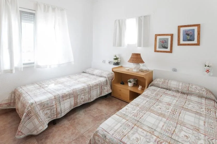 A bright bedroom with two beds and a wooden bedside table.