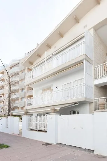 Un edificio blanco de varias plantas con balcones está junto a un camino pavimentado.