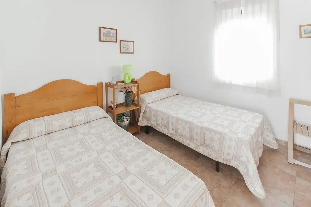 Un dormitorio con dos camas y una pequeña estantería junto a ellas.