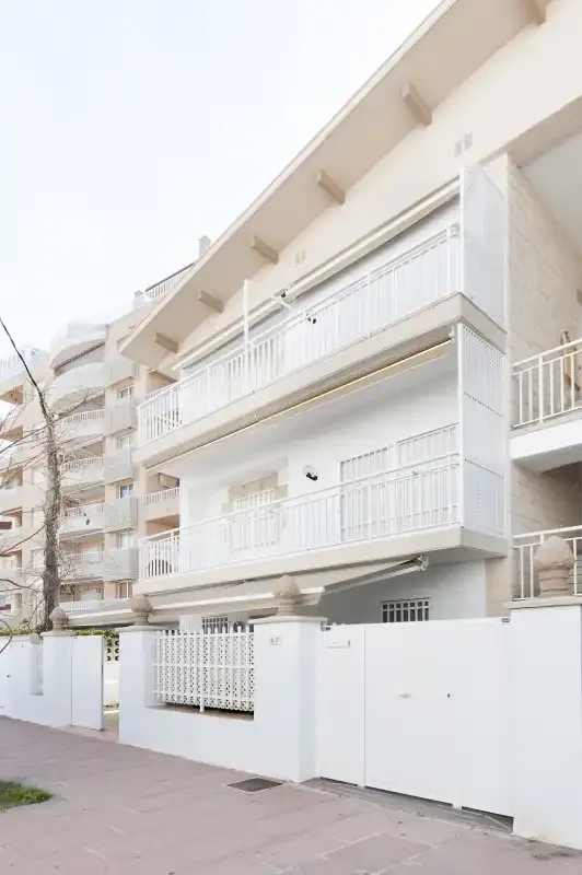Un edificio blanco de varias plantas con balcones se alza tras un muro bajo.