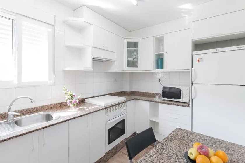 A bright kitchen with white cabinets, a sink, and a refrigerator.