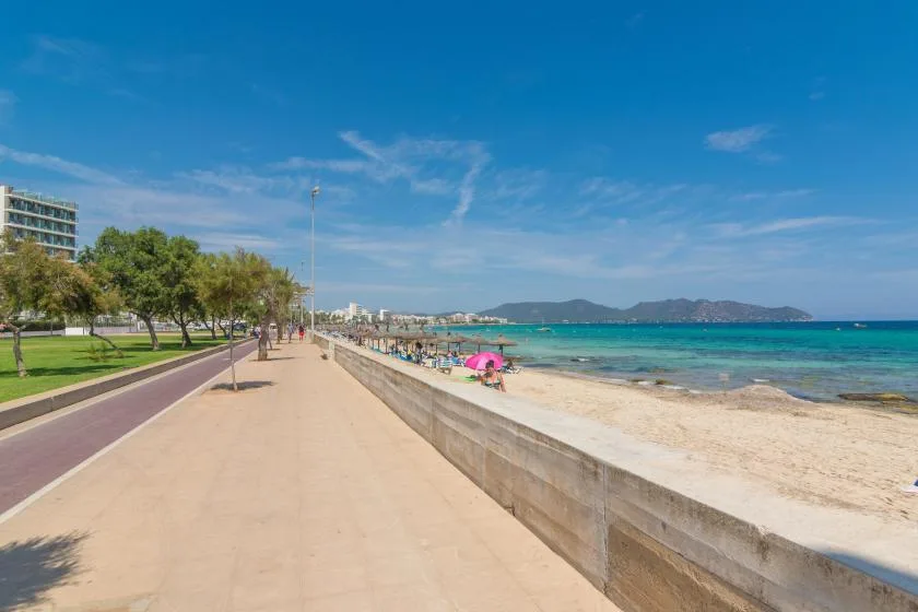 A seaside promenade runs beside a sandy beach and clear blue water.