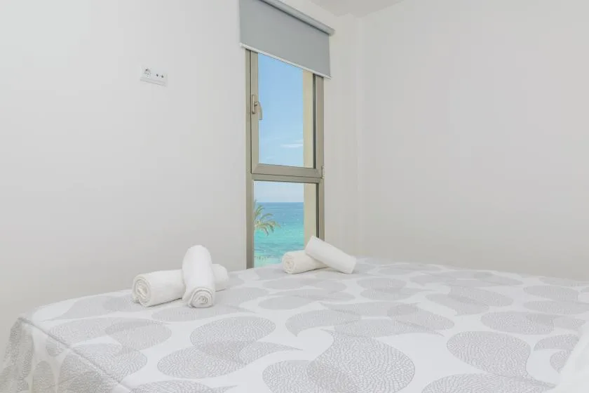 A bedroom with a neatly made bed and a window overlooking the sea.