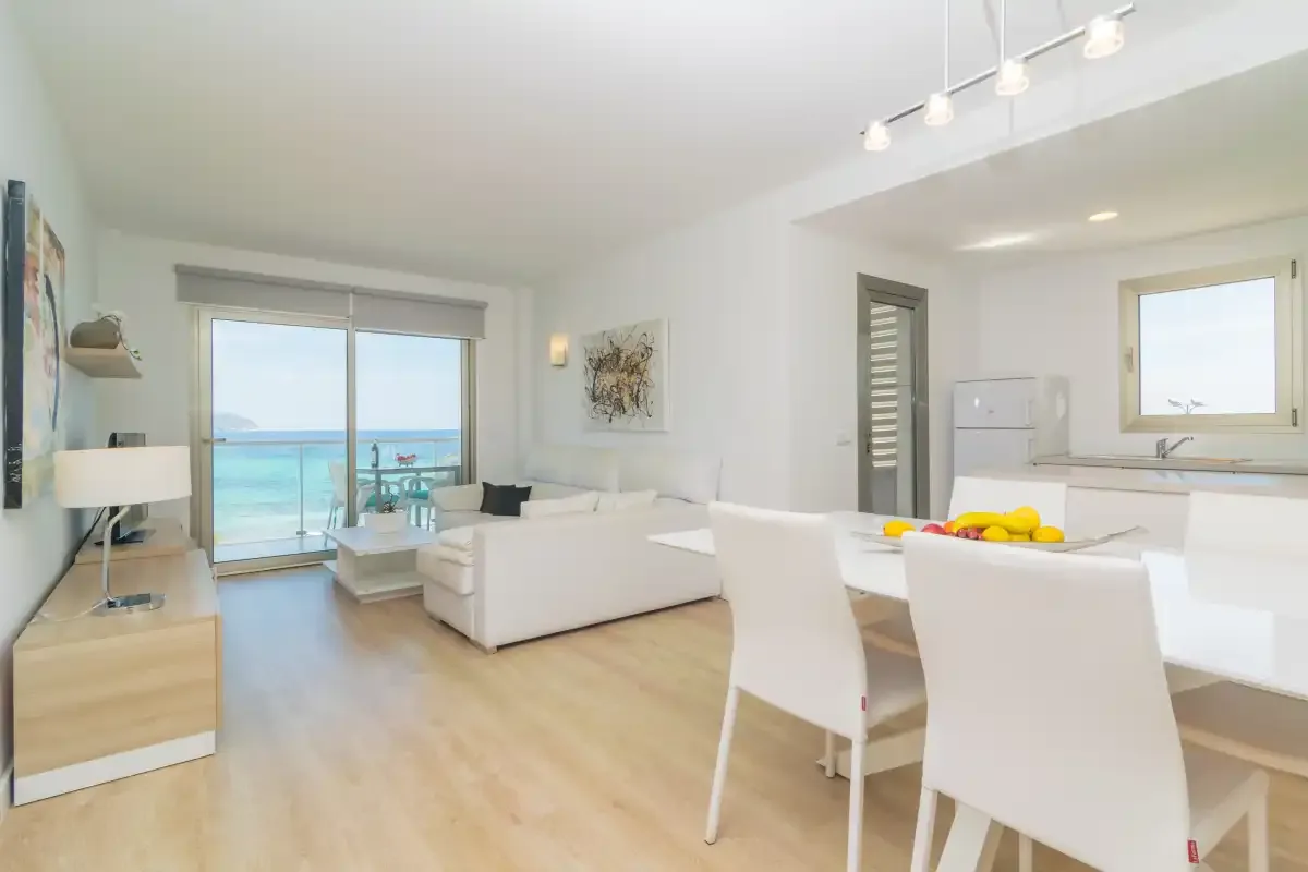 Bright living and dining area with white seating and a view of the sea.