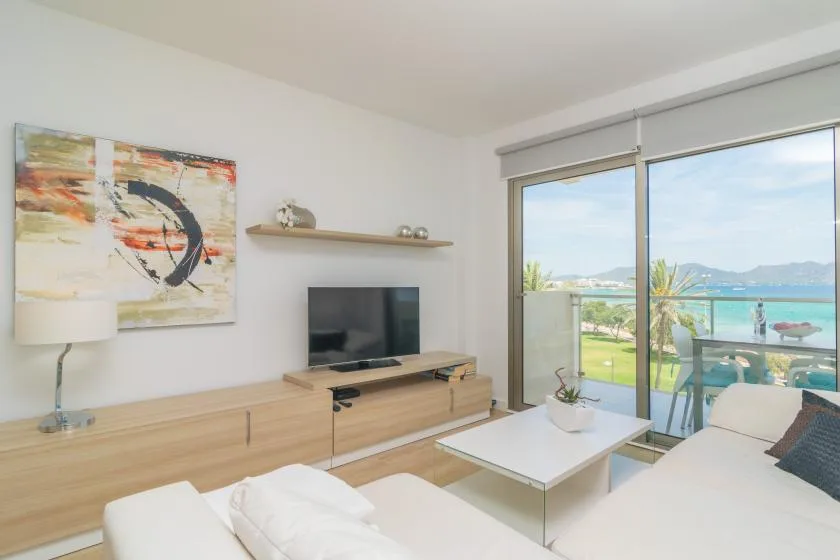 A bright living room with seating, a television, and sliding glass doors overlooking the water.