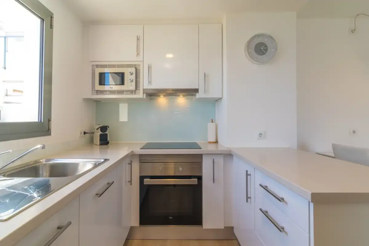 A bright kitchen with white cabinets, a built-in oven, and a sink.