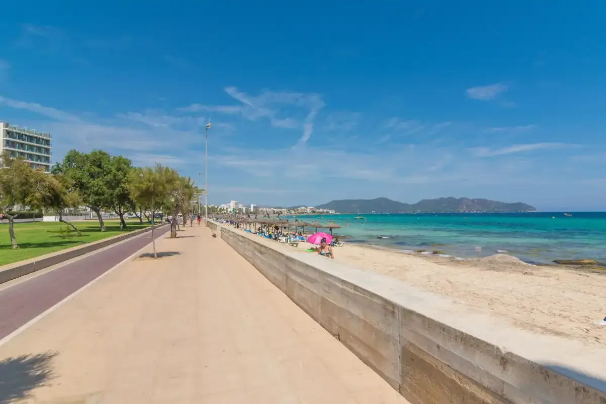 A seaside promenade runs beside a sandy beach and turquoise water.