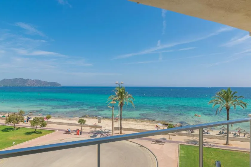 A seaside view from a balcony overlooks turquoise water, a beach, and palm trees.