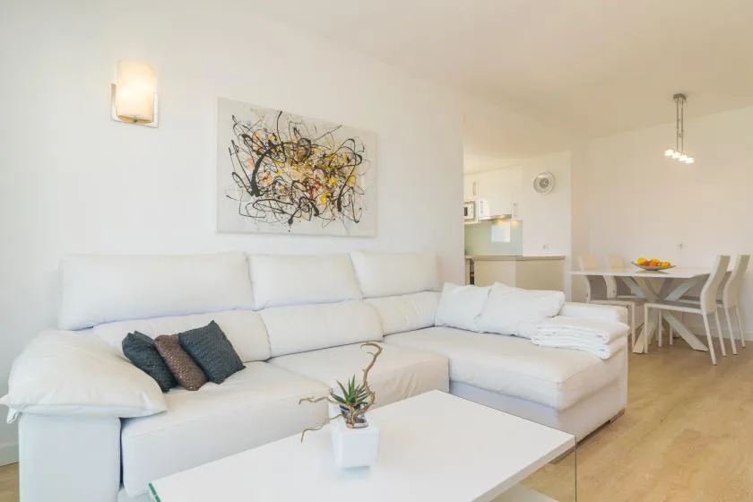 A bright living and dining area with white seating and a table beneath abstract wall art.