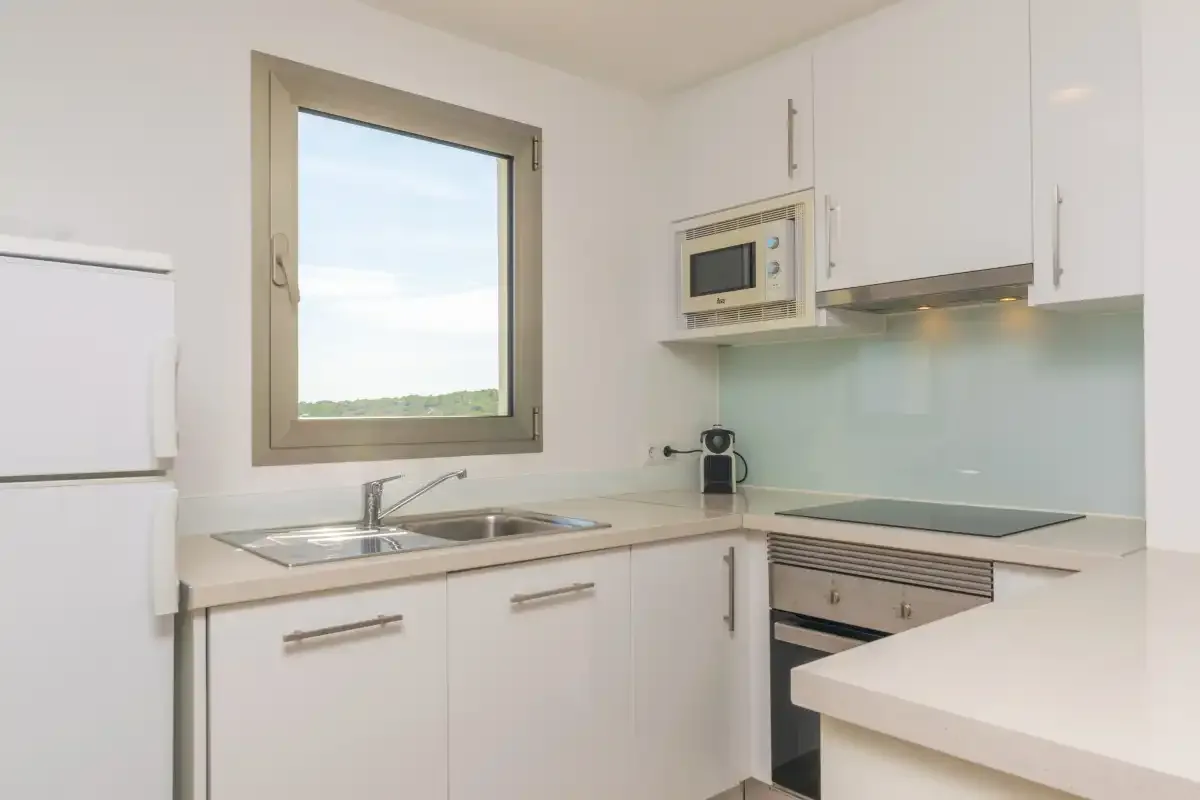 A bright kitchen with white cabinets, a sink, and a cooktop.