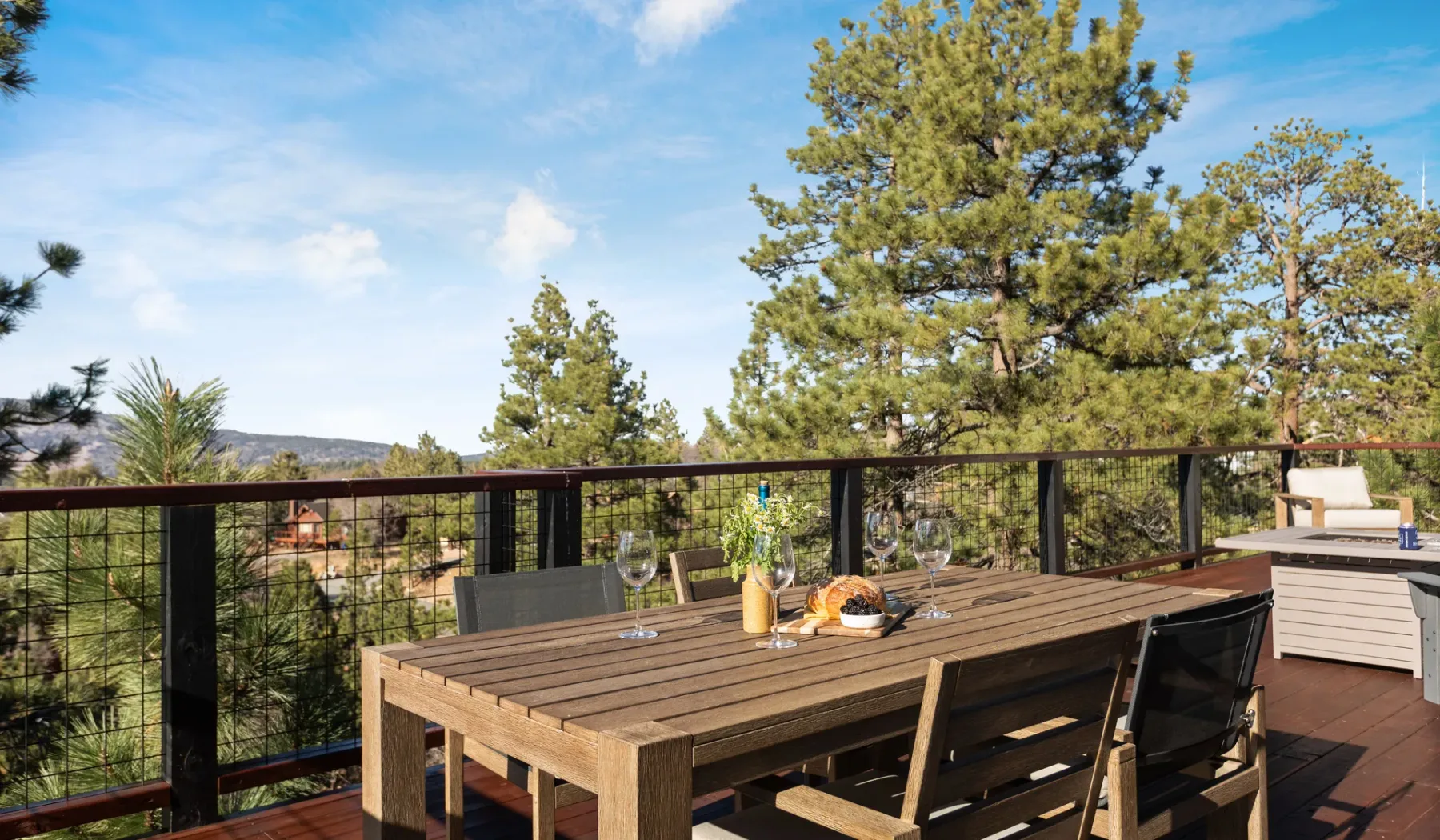 Una mesa de comedor de madera está en una terraza con vistas a árboles y colinas lejanas.